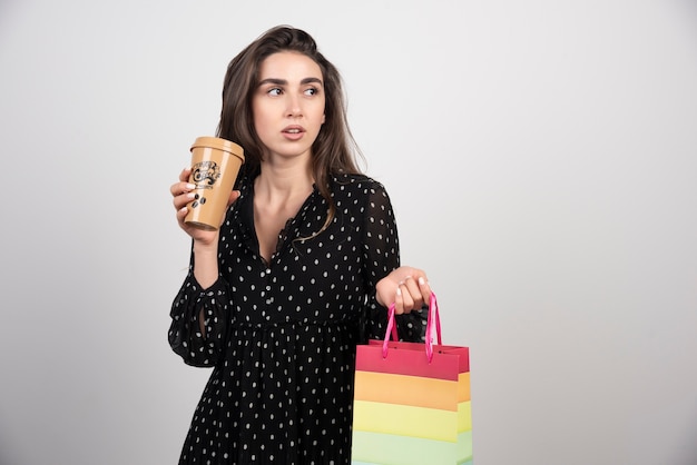 Modello della giovane donna che tiene una borsa del negozio con una tazza di caffè