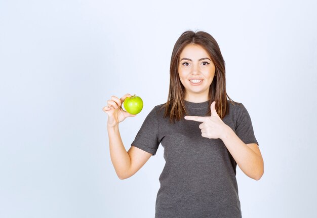 модель молодой женщины, указывая на зеленое яблоко.