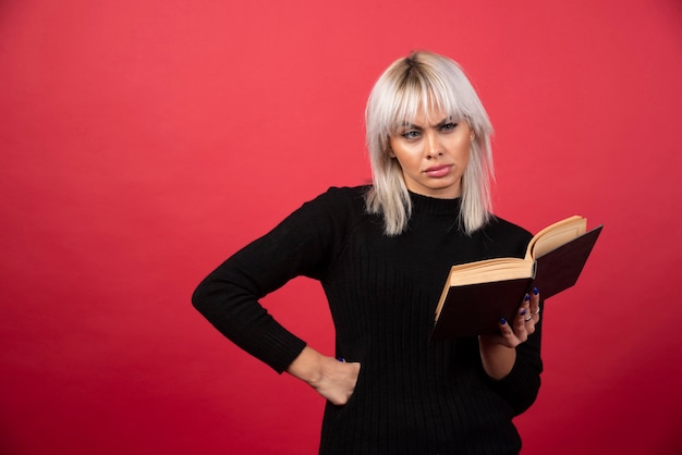 Бесплатное фото Модель молодой женщины, читая книгу на красной стене.