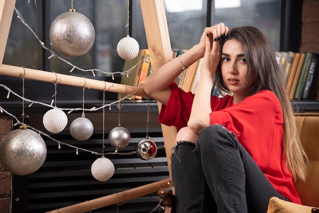Foto gratuita un modello di giovane donna in camicia rossa seduta e in posa.