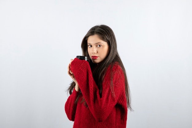 A young woman model in red sweater holding a cup of coffee