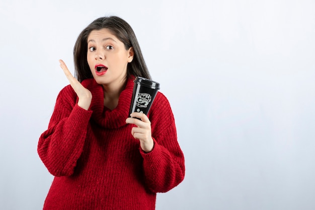 A young woman model in red sweater holding a cup of coffee