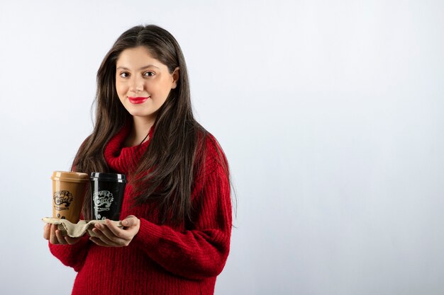 A young woman model in red sweater holding two cups of coffee