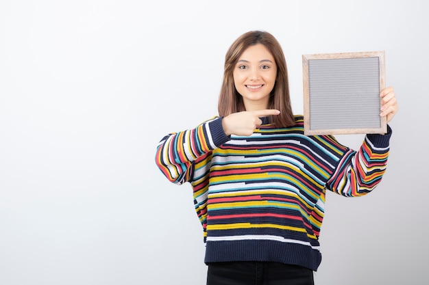 young woman model standing and pointing at a frame.