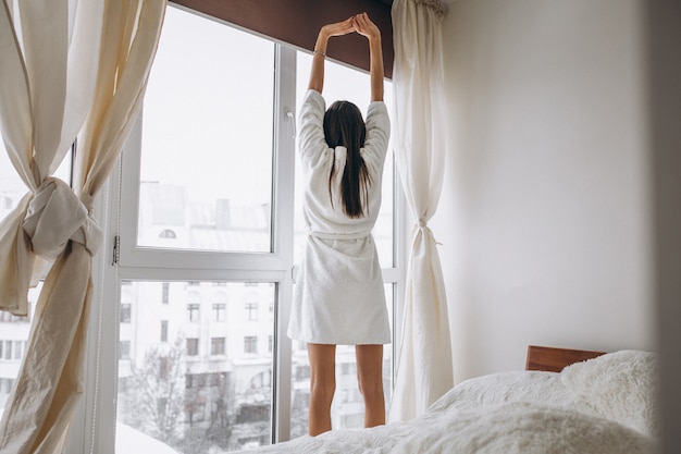Молодая женщина утром растягивается у окна