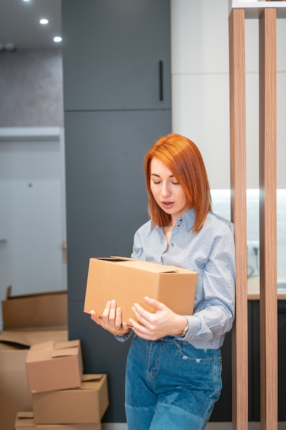 Молодая женщина переезжает в новую квартиру с картонными коробками
