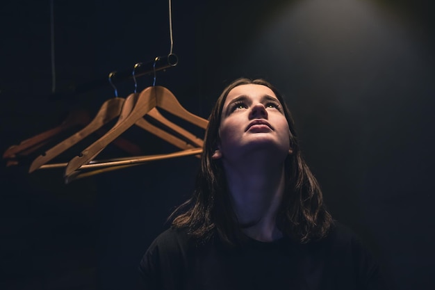 A young woman near empty hangers in the dark under a lamp