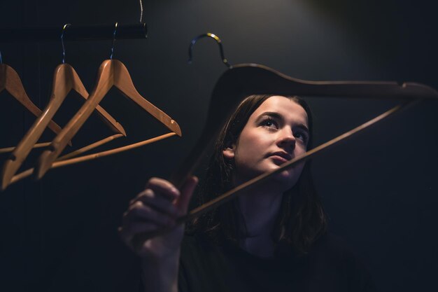 Free photo a young woman near empty hangers in the dark under a lamp