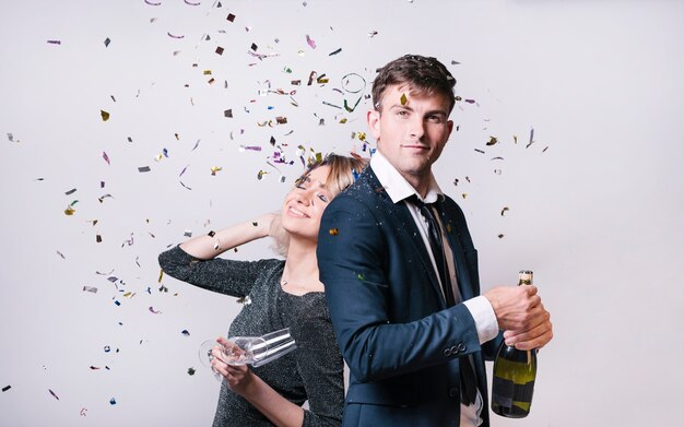 Young woman near man with bottle of drink between tossing confetti