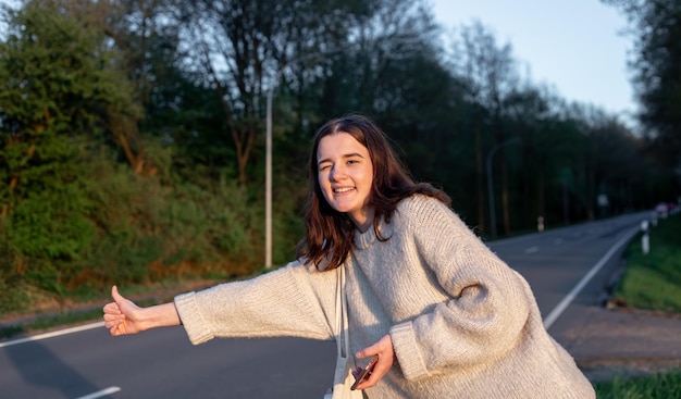 Free photo a young woman near the road stops the car hitchhiking