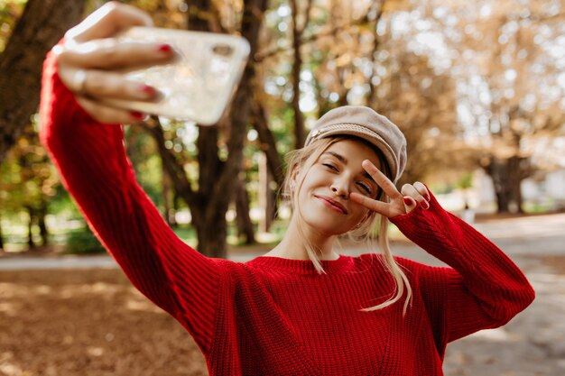 좋은 빨간 스웨터에 젊은 여자는 공원 경로에 selfie를 확인합니다.