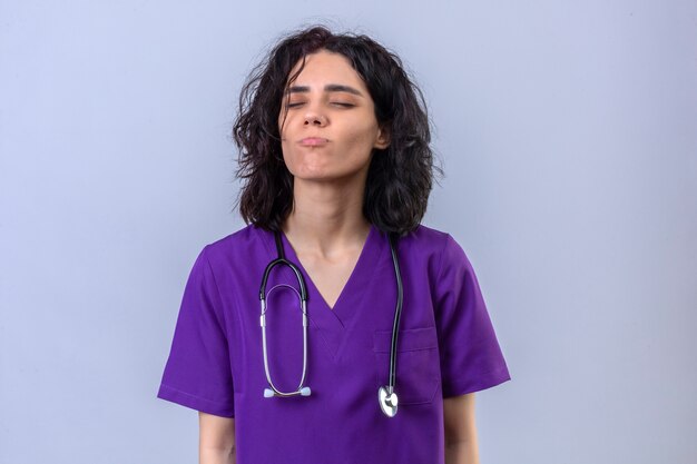 Young woman nurse in medical uniform and with stethoscope looking confident and proud standing with closed eyes blowing a kiss standing