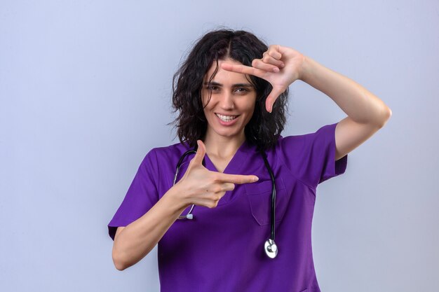 Young woman nurse in medical uniform and with stethoscope making a frame gesture with hands