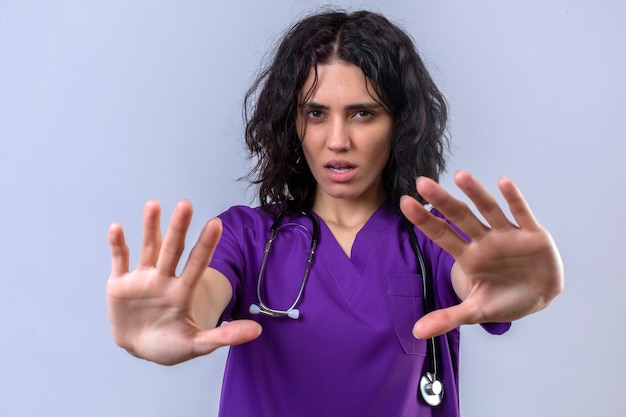 Free photo young woman nurse in medical uniform and with stethoscope scared holding her hands up telling do not come closer