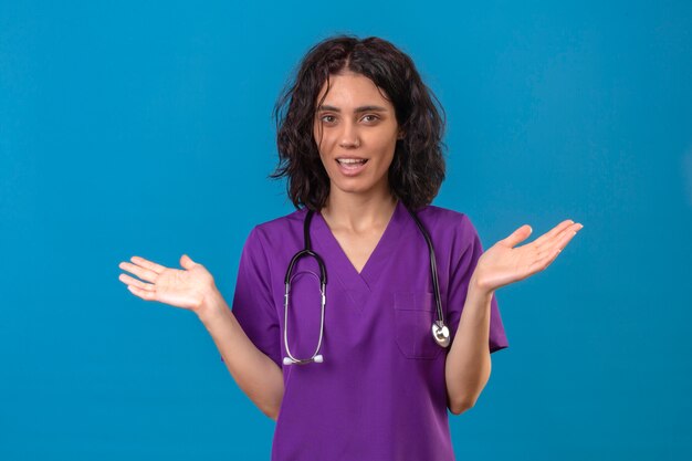 젊은 여자 간호사 의료 유니폼과 청진 어깨를 으쓱하는 불확실하고 혼란스러워 보이는 대답이 서있는