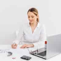 Free photo young woman in office doing paperwork in front of laptop