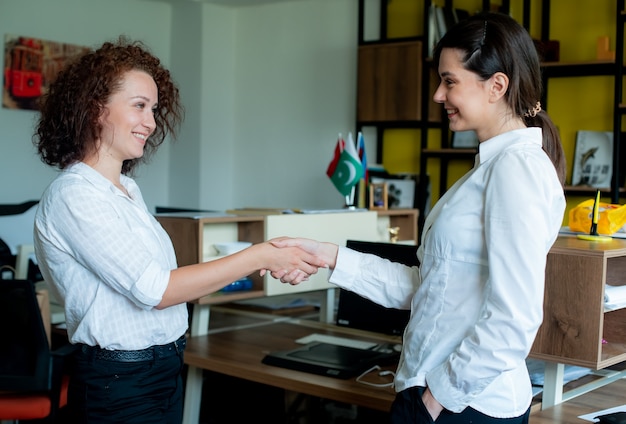 Foto gratuita giovane donna impiegato sorridente amichevole stringe la mano con il collega in piedi in ufficio