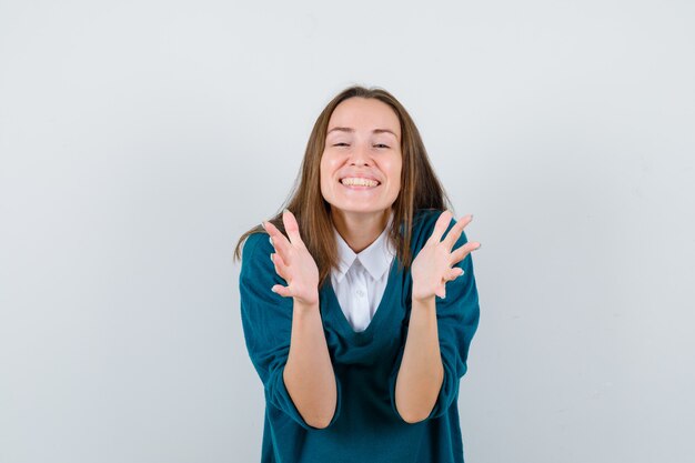 Молодая женщина раскрывает руки для объятия в свитере над белой рубашкой и выглядит счастливым, вид спереди.