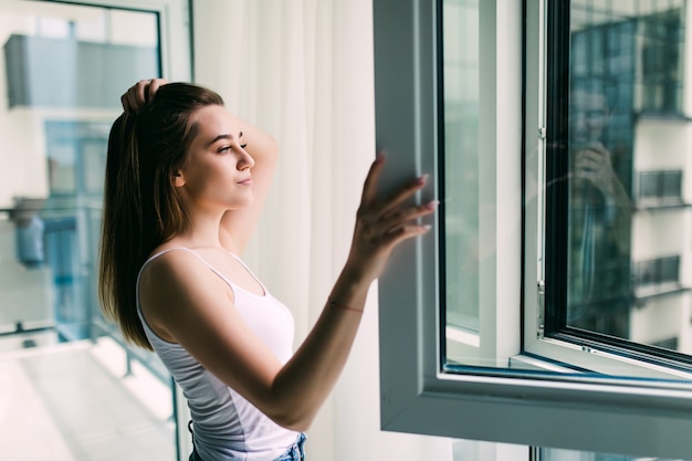 Young woman opens a plastic window for fresh air and smiling at home