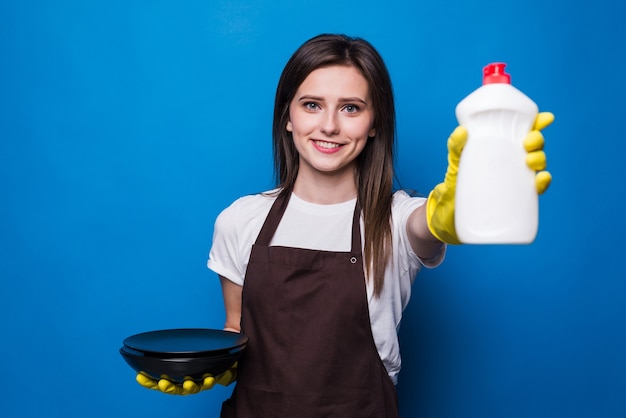 分離されたスポンジと食器用洗剤を示す洗浄プレートとオレンジ色のエプロンの若い女性。保護手袋、食器用洗剤、スポンジ-食器洗いに最適