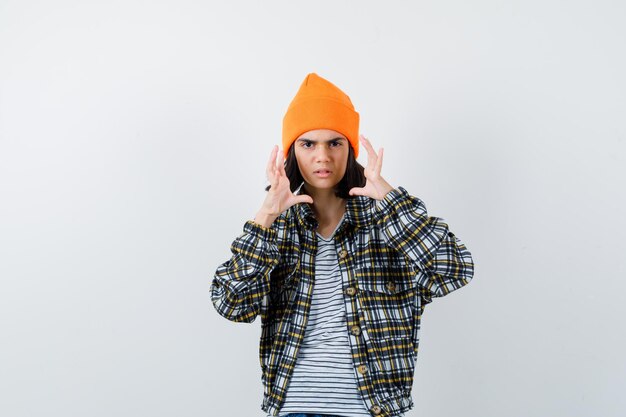 Young woman in orange hat checkered shirt holding hands near face looking upset