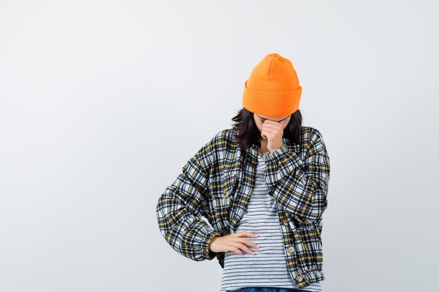 Free photo young woman in orange hat and checkered shirt leaning head on hand and looking upset