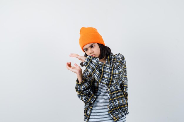 深刻に見える何かを保持しているふりをしているオレンジ色の帽子の市松模様のシャツの若い女性