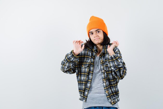 Young woman in orange hat and checkered shirt standing shrugging shoulders