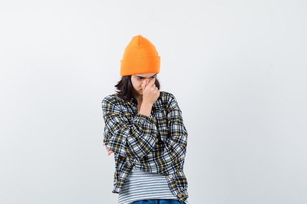 Young woman in orange hat holding hand on nose looking sad