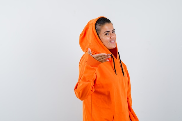 Young woman in orange hoodie stretching hand toward camera and looking happy 