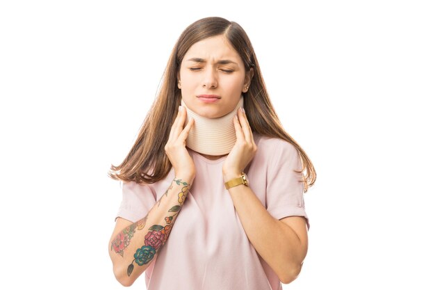 Young woman in pain wearing cervical collar over white background