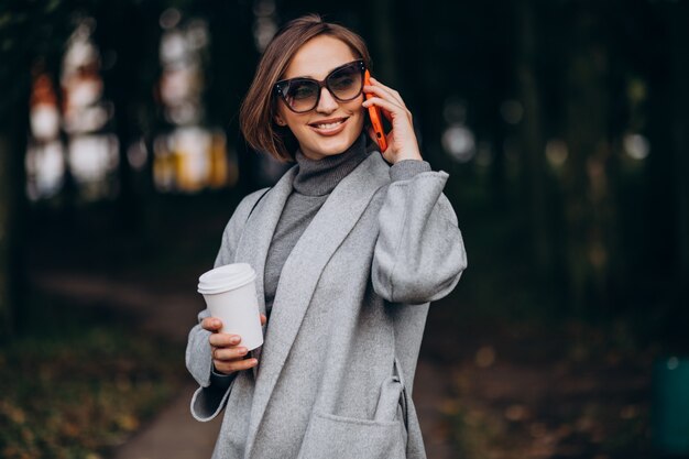 コーヒーを飲み、電話で話している公園の若い女性