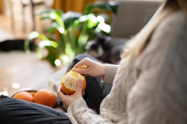 Young woman peeling an orange on the sofa