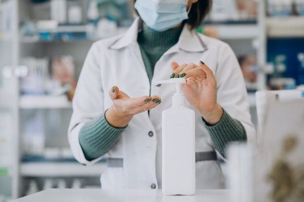 Young woman pharmacist desinfecting hands with sanitazer