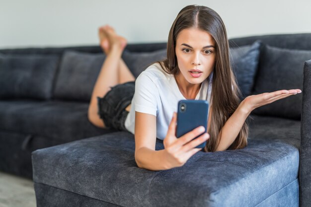Young woman phone user having video call. Young woman in casual lying on couch, using smartphone and smiling at screen.