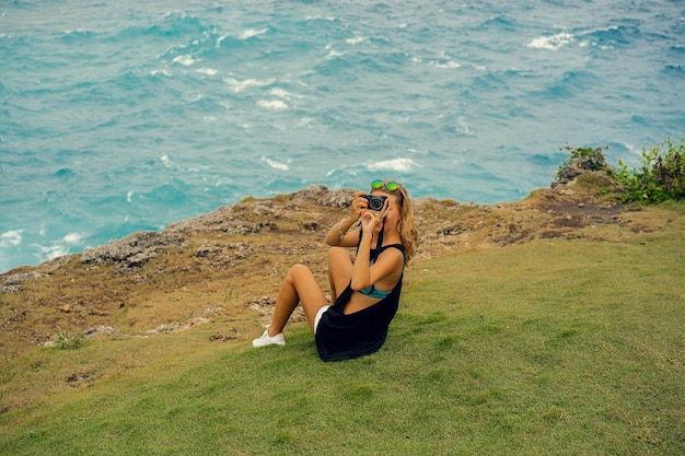 Free photo young woman photographer traveler with a camera on the edge of a cliff takes pictures of nature