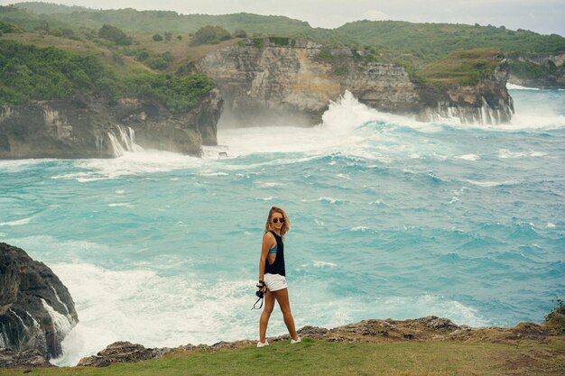 Young woman photographer traveler with a camera on the edge of a cliff takes pictures of nature