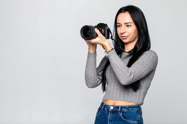 Young woman photographer with camera isolated on gray wall