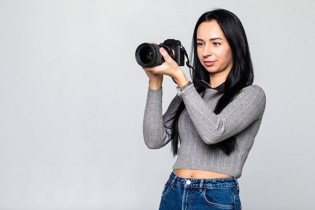 灰色の壁に分離されたカメラを持つ若い女性写真家
