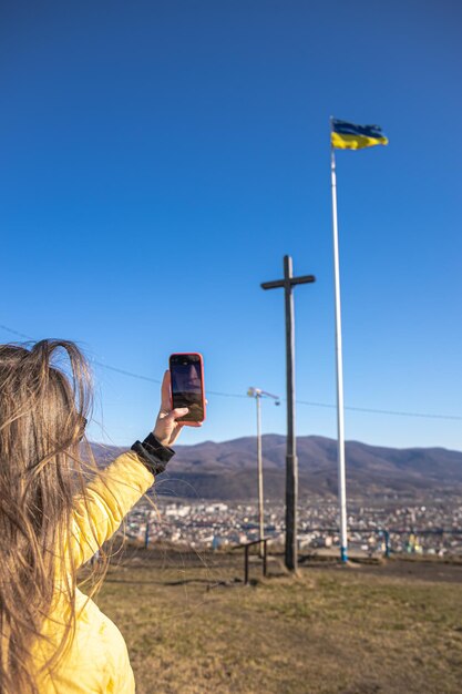 A young woman photographs the flag of ukraine against the backdrop of the city