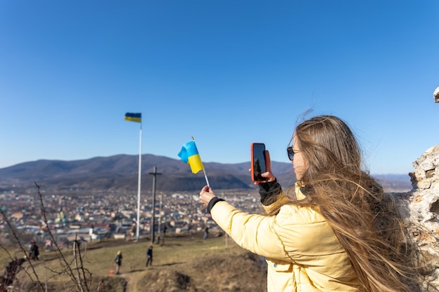 Молодая женщина фотографирует флаг украины на фоне города