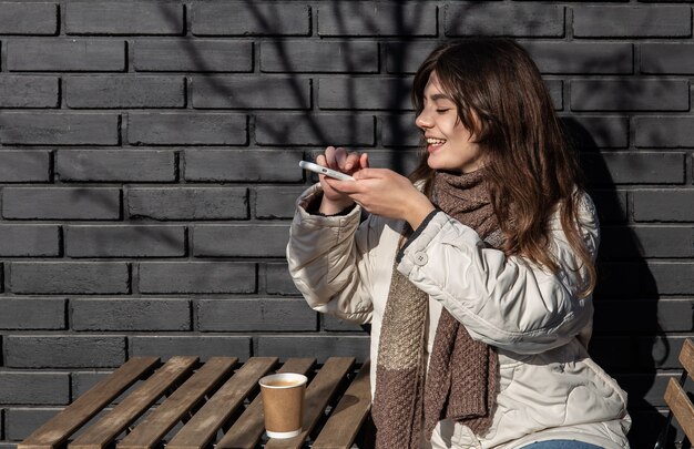 若い女性が街の散歩で温かい飲み物のグラスを撮影します