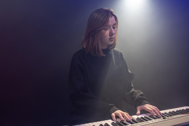 Young woman pianist plays the keys in a dark room with haze