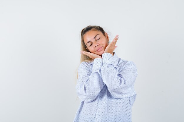 Young woman pillowing face on hands, keeping eyes closed in white shirt and looking cute