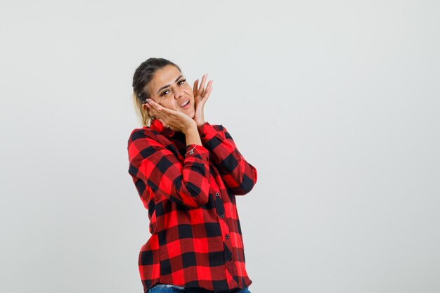 Young woman pillowing face on her hands in checked shirt and looking cute , front view.