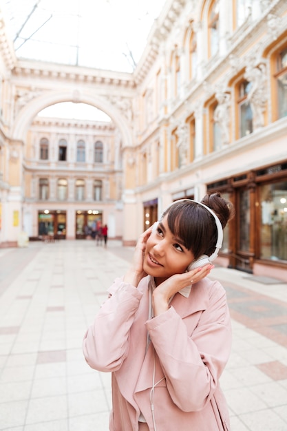 外のヘッドフォンで音楽を聴くピンクのコートの若い女性