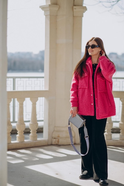 通りに立っているピンクのコートを着た若い女性