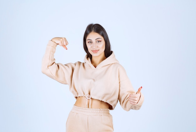 Young woman in a pink hoodie showing her muscles