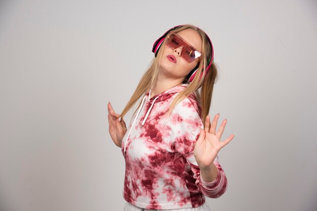 Young woman in pink outfit dancing on gray background.