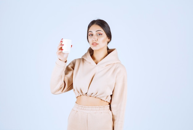 Молодая женщина в розовой пижаме держит чашку напитка